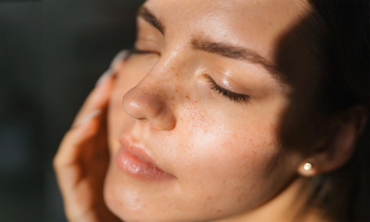 A close-up of a woman's face with natural freckles, glowing skin, and soft light emphasizing her serene expression - Brow Lift in West Hollywood, CA