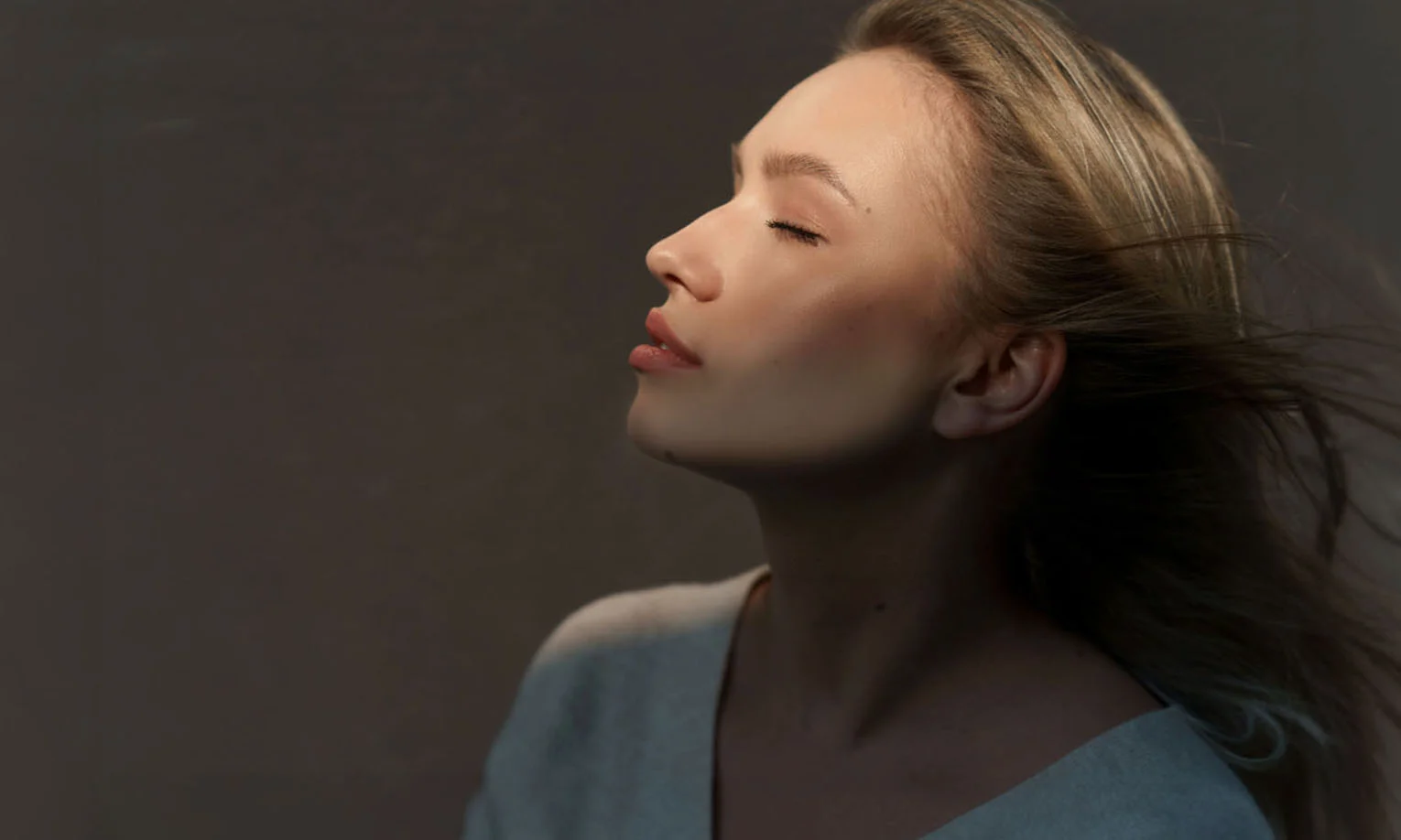 Graceful woman in soft lighting, highlighting her serene side profile with eyes closed - Facial Reshaping in West Hollywood, CA