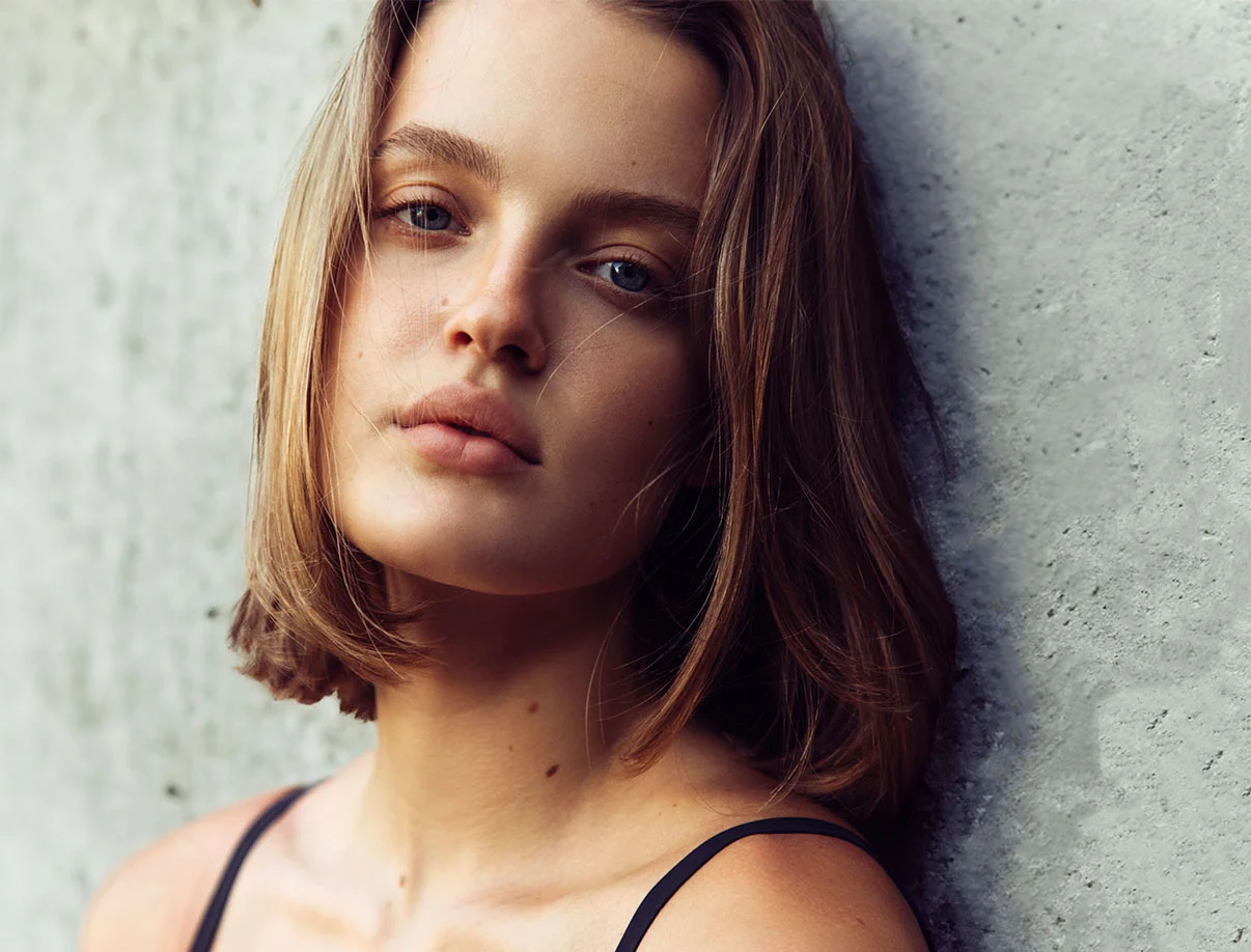 Close-up of a woman standing against a textured wall, gazing softly at the camera - Lip Lift in West Hollywood, CA