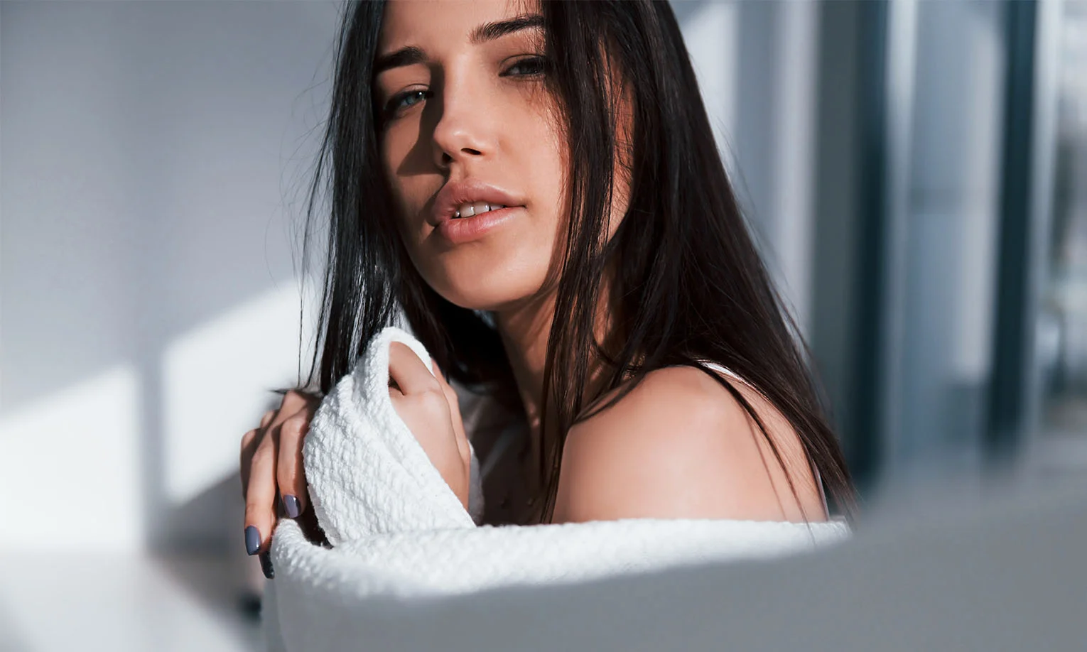 A young woman with long dark hair poses softly, wrapped in a white towel, with natural light illuminating her face. - Microneedling PRP as add ons in West Hollywood, CA