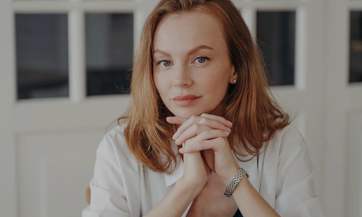 A confident woman with light red hair, resting her chin on her hands, exuding a calm and thoughtful demeanor - Stelar Banking in West Hollywood, CA