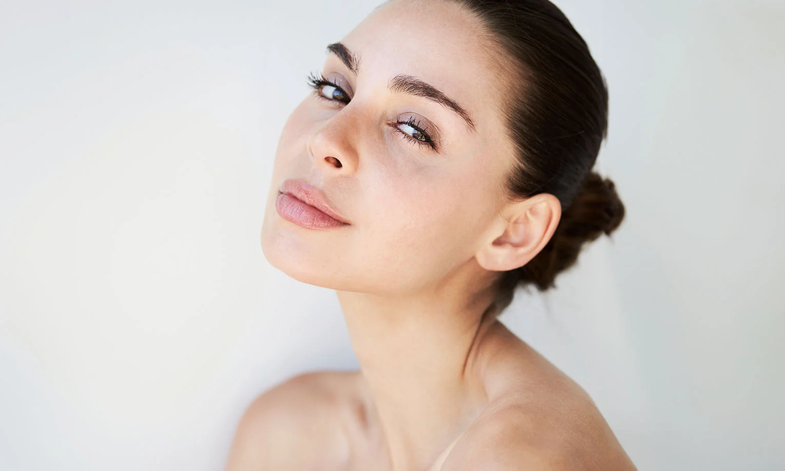 A woman with a natural look poses serenely, facing slightly to the side, against a soft, light background. - Stem Cell Face Lift in West Hollywood, CA